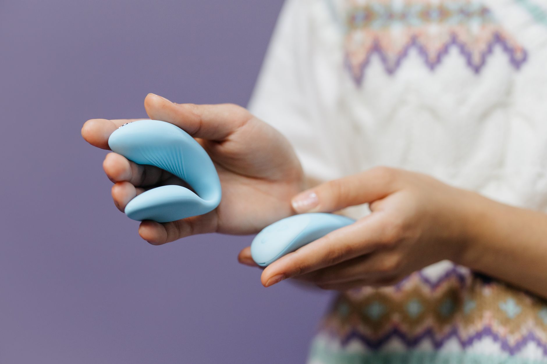 A hand holding a sleek blue lemon clitoral vibrator against a purple background