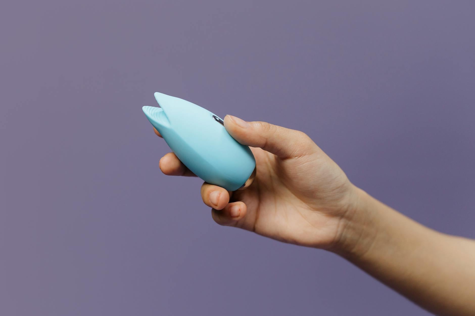 Vibrador de silicone azul seguro na mão contra fundo roxo sólido, promovendo amor-próprio e sexualidade