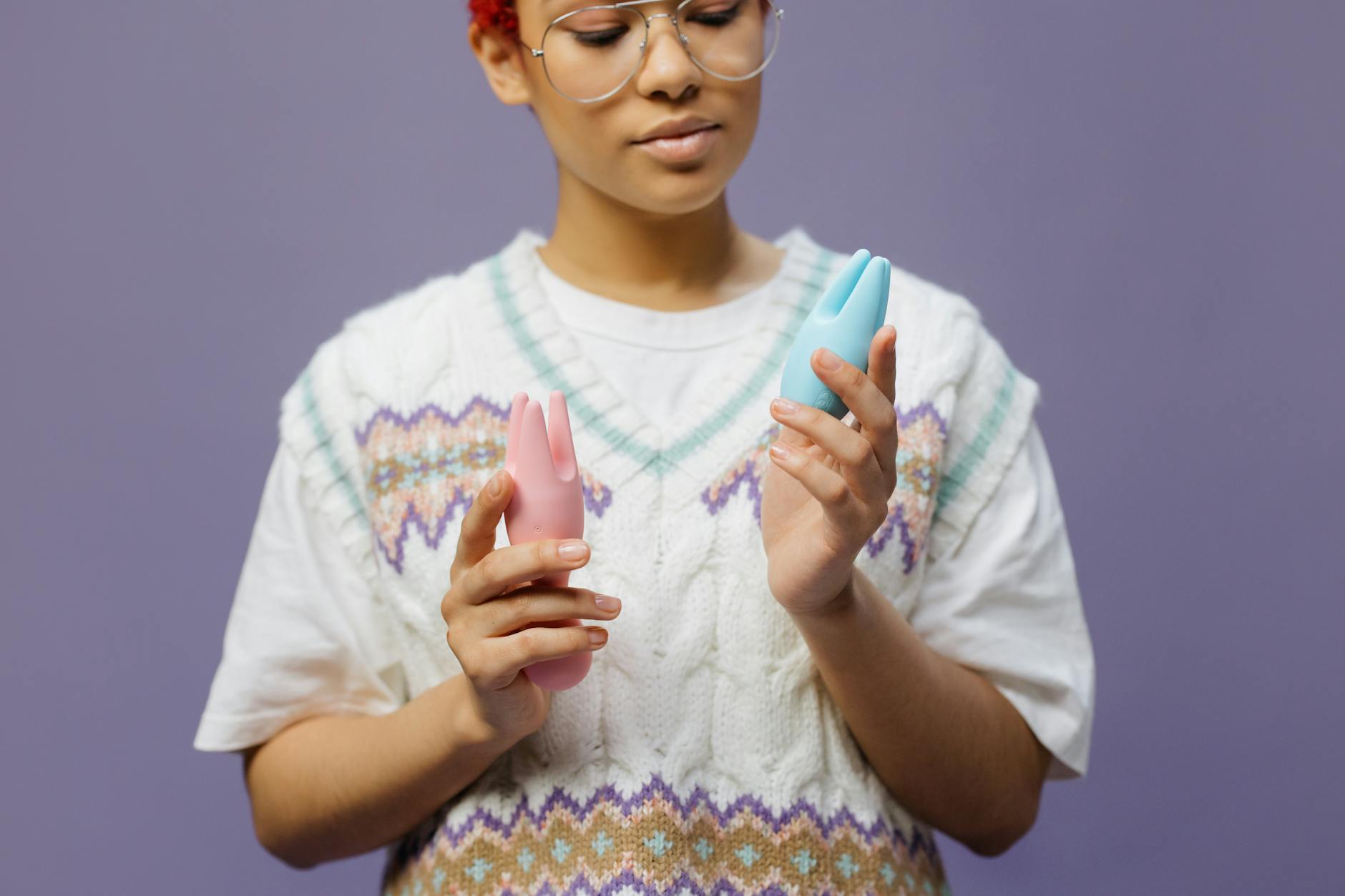 Mulher segurando vibradores de silicone rosa e azul com expressão contemplativa