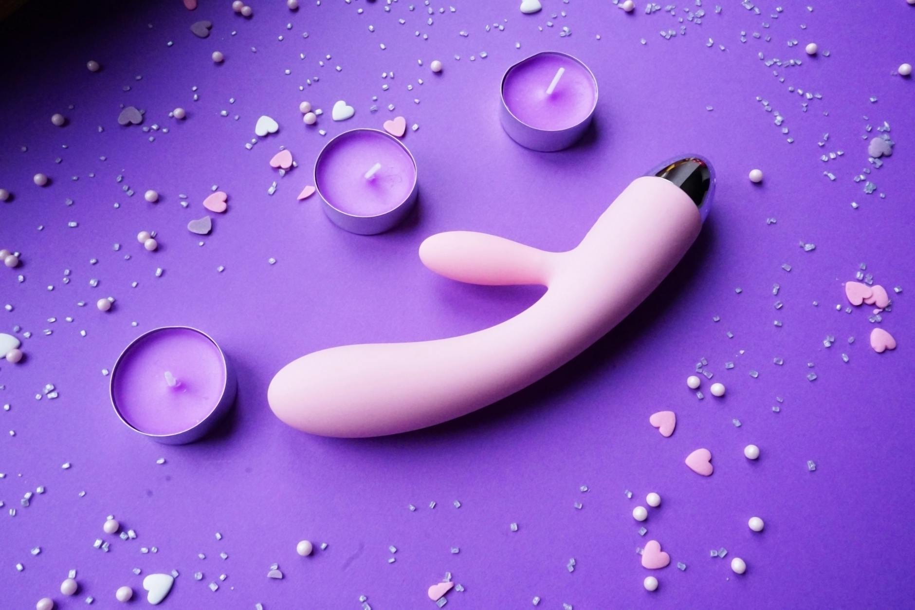 Pink vibrator on purple background with romantic candles and confetti