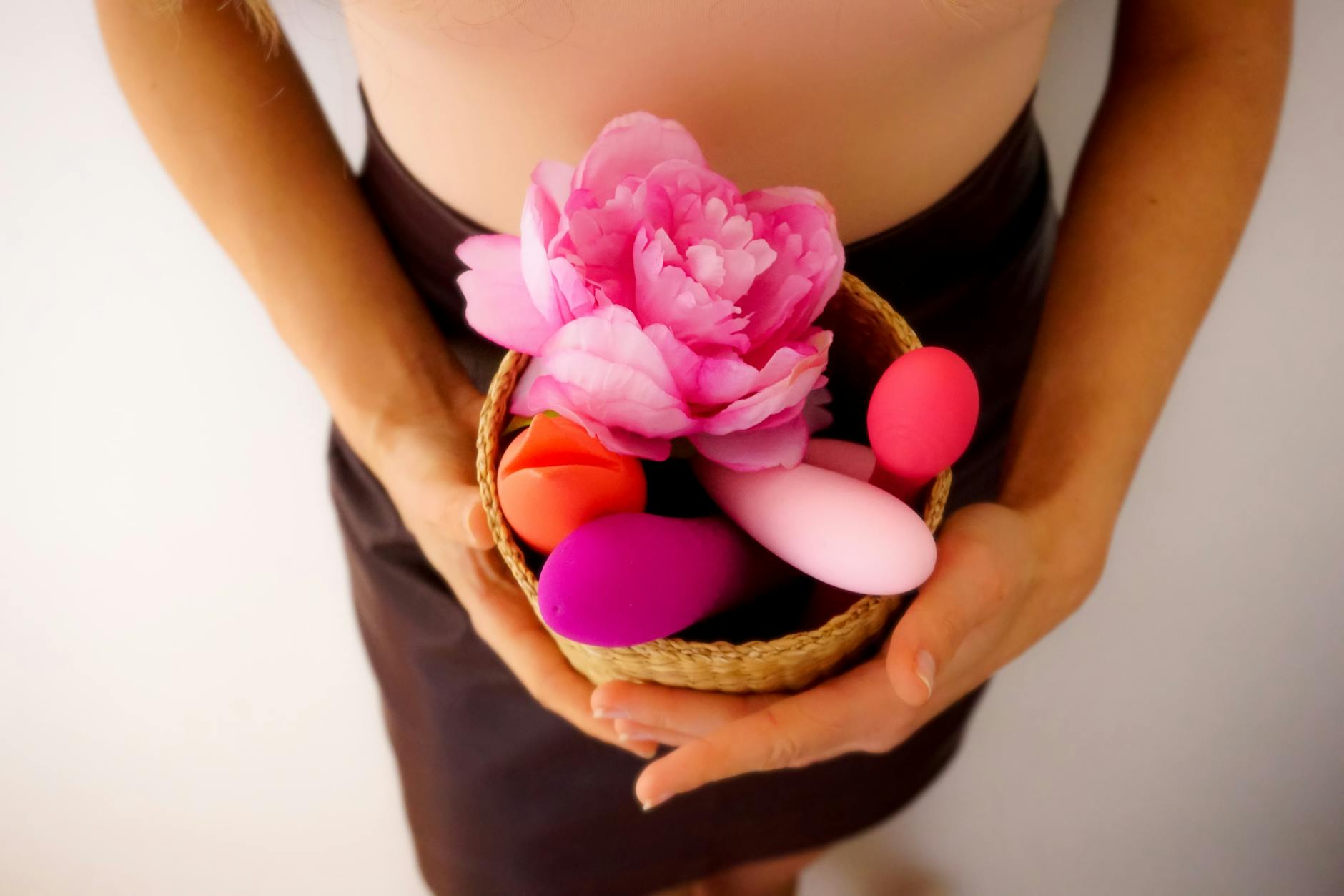 Cesta com vibradores coloridos e flor rosa, representando exploração de prazer e bem-estar sensual